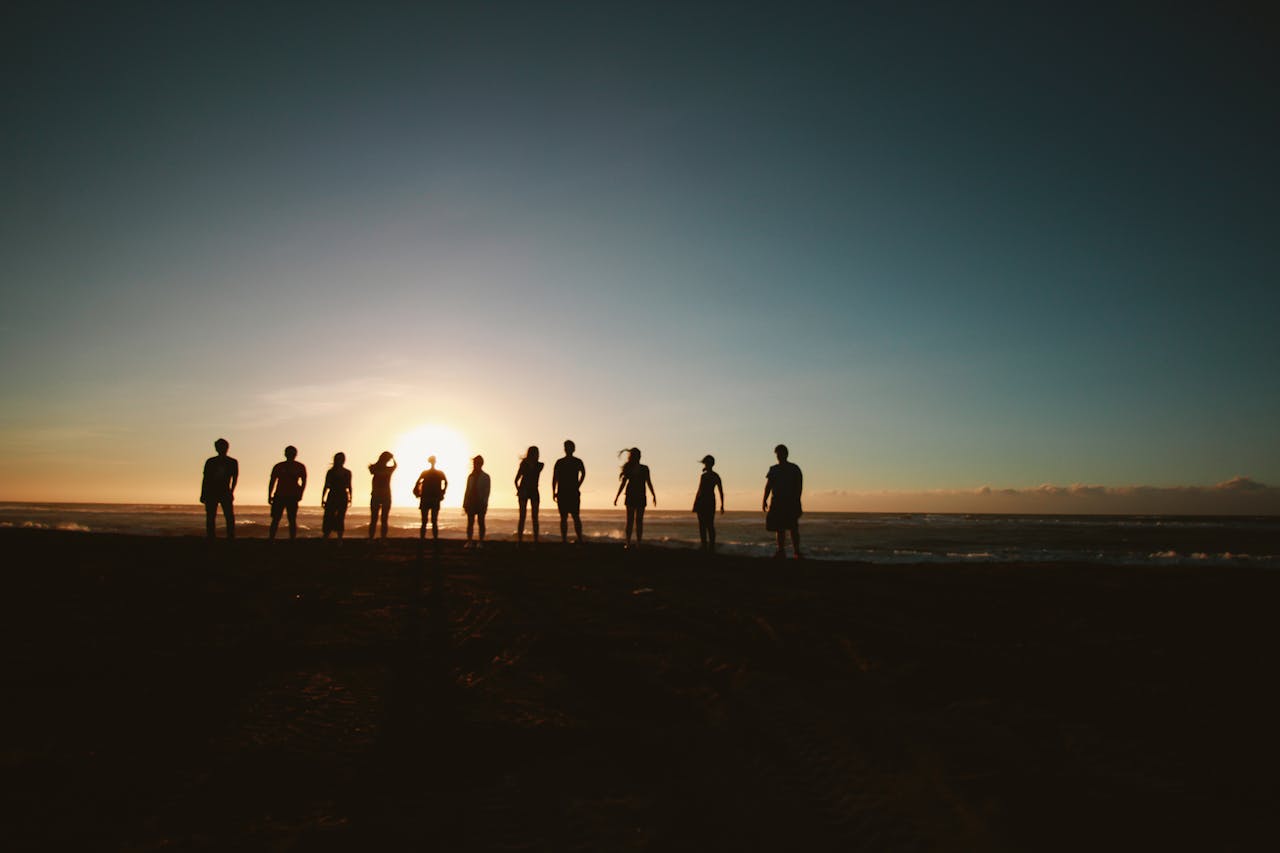 A group of friends standing on a beach, silhouetted against a vibrant sunset over the ocean.